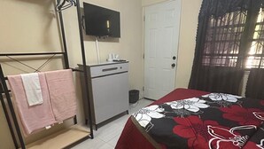 Ein Schlafzimmer mit Bett, Schreibtisch, Fernseher, Kleiderschrank und einer Tür.