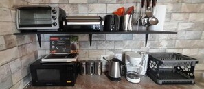 A kitchen with a microwave, toaster, coffee maker, and various utensils on shelves.
