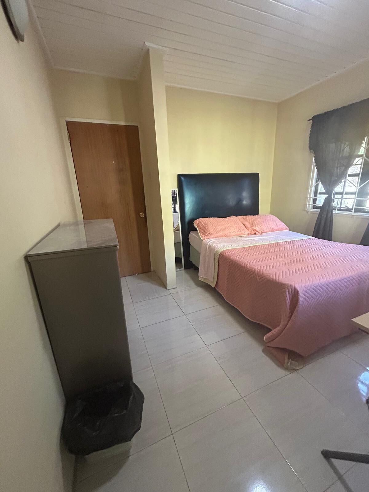 A bedroom with a bed, a desk, and a window with curtains.