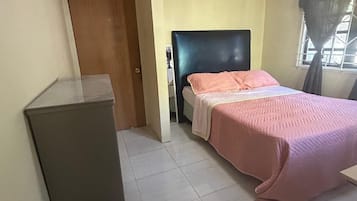 A bedroom with a bed, a desk, and a window with curtains.