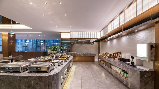 A modern breakfast bar with buffet-style food stations, a coffee machine, and a large window with curtains. - Crystal Hotel Qingdao Shilaoren Beach (Qingdao)