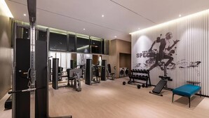 A gym with weight machines, a bench, and a wall with a large abstract design. - Crystal Hotel Qingdao Shilaoren Beach (Qingdao)