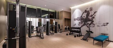 Un gimnasio con máquinas de pesas, una banca y una pared con un diseño abstracto grande.