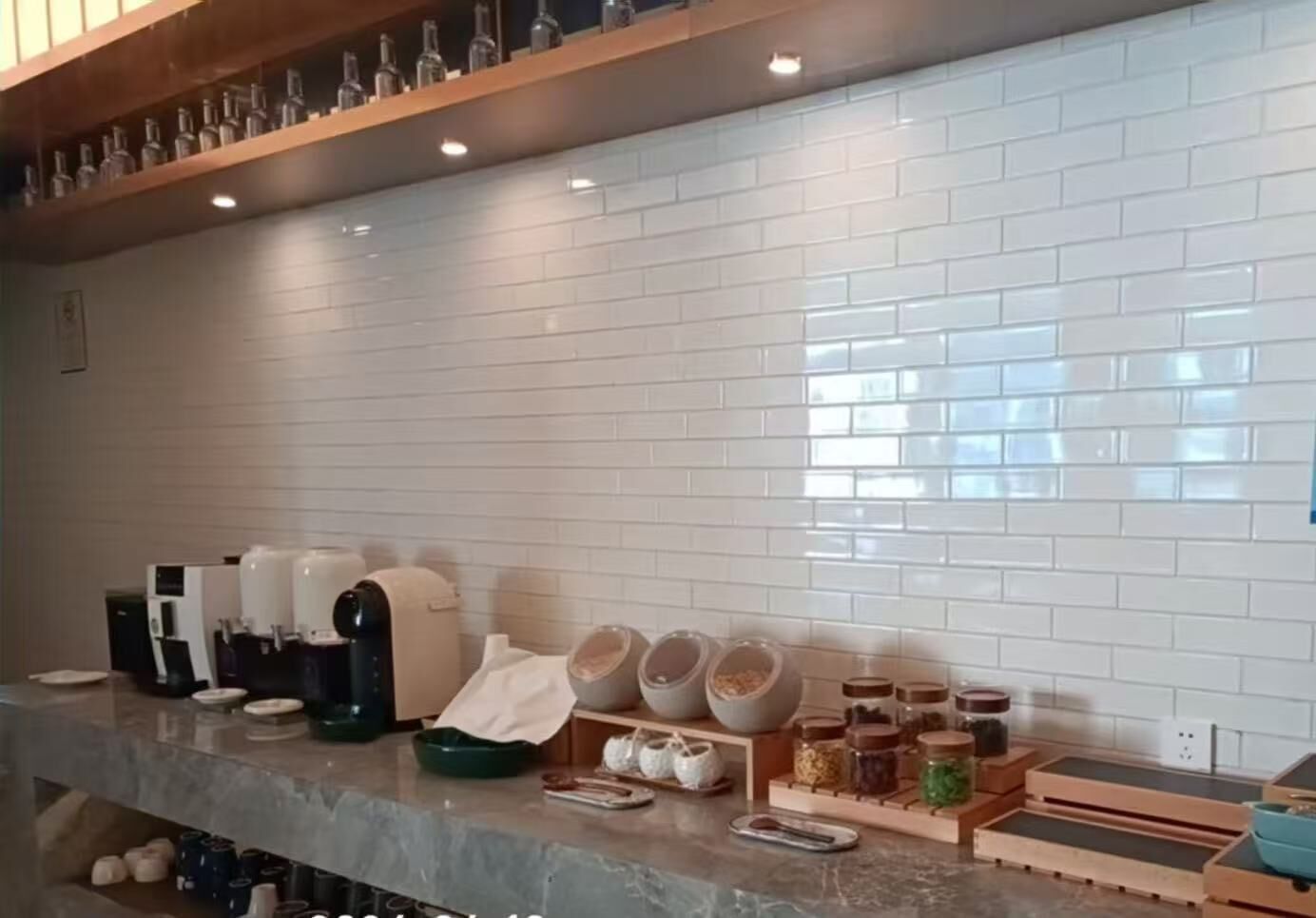 Uma cozinha com painel de azulejos brancos, máquinas de café, potes e bancada de mármore.