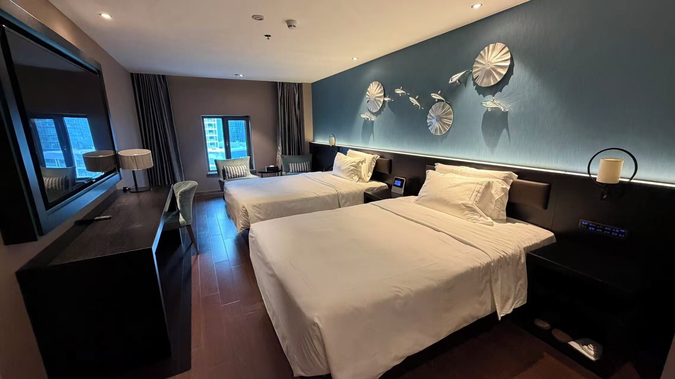 A hotel room with two beds, a desk, a chair, a TV, and decorative wall art.