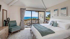 Ein Schlafzimmer mit einem großen Bett, einem grünen Sessel, einem Deckenventilator und Meerblick durch eine Glasschiebetür.