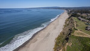Ein Hotel an der Küste mit Blick auf den Strand, einem Sandstrand und einer hügeligen Landschaft im Hintergrund.