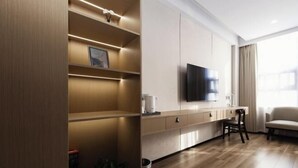 A modern hotel room with a wooden floor, a flat-screen TV mounted on the wall, a sofa, a dining table with chairs, and built-in shelves with a picture frame. - Academic Exchange Center of Central China Normal University (Guiyuan Hotel) (Wuhan)