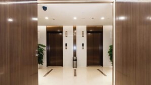 An elevator area with two elevators, a trash bin, and potted plants. - Academic Exchange Center of Central China Normal University (Guiyuan Hotel) (Wuhan)