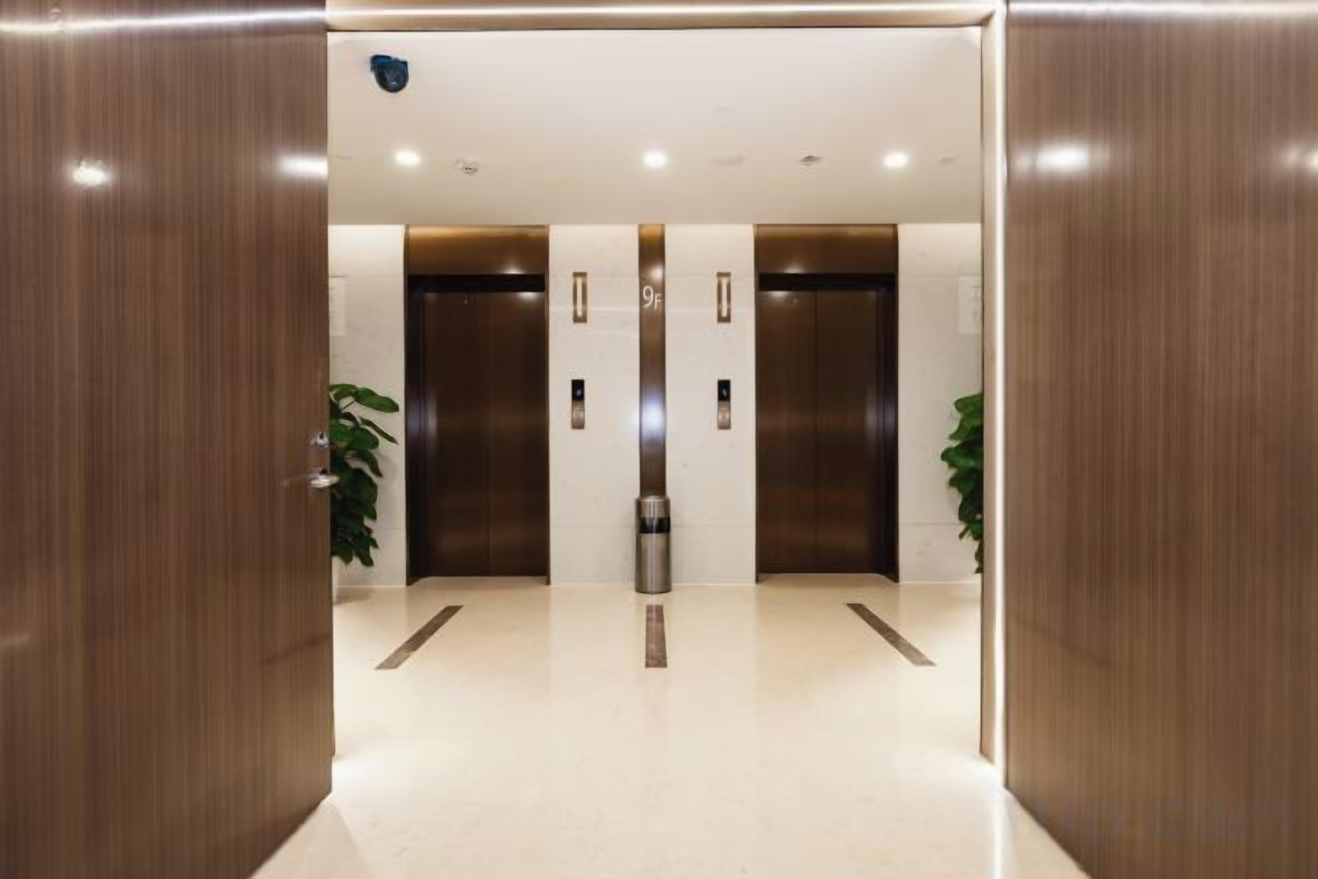 A modern elevator area with two elevators, a trash bin, and potted plants.