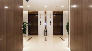 A modern elevator area with two elevators, a trash bin, and potted plants.