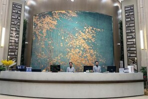 A reception desk with a large mural of a tree and leaves, two receptionists, and a counter with various items. - Academic Exchange Center of Central China Normal University (Guiyuan Hotel) (Wuhan)