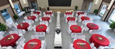 A conference room with rows of tables and chairs, a large screen at the front, and potted plants.