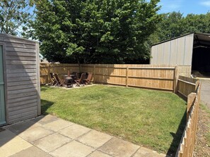 Ein Garten mit Holzzaun, Grill und Gartenhaus.