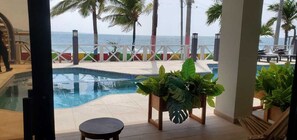A pool area with a view of the ocean, surrounded by palm trees and lounge chairs. - Litos Hotel y Restaurante (La Libertad)