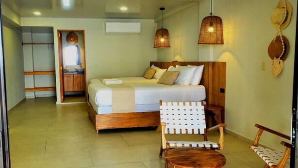 Ein Schlafzimmer mit einem hölzernen Bett, einem kleinen Tisch, einem Stuhl und Meerblick durch eine Glastür.