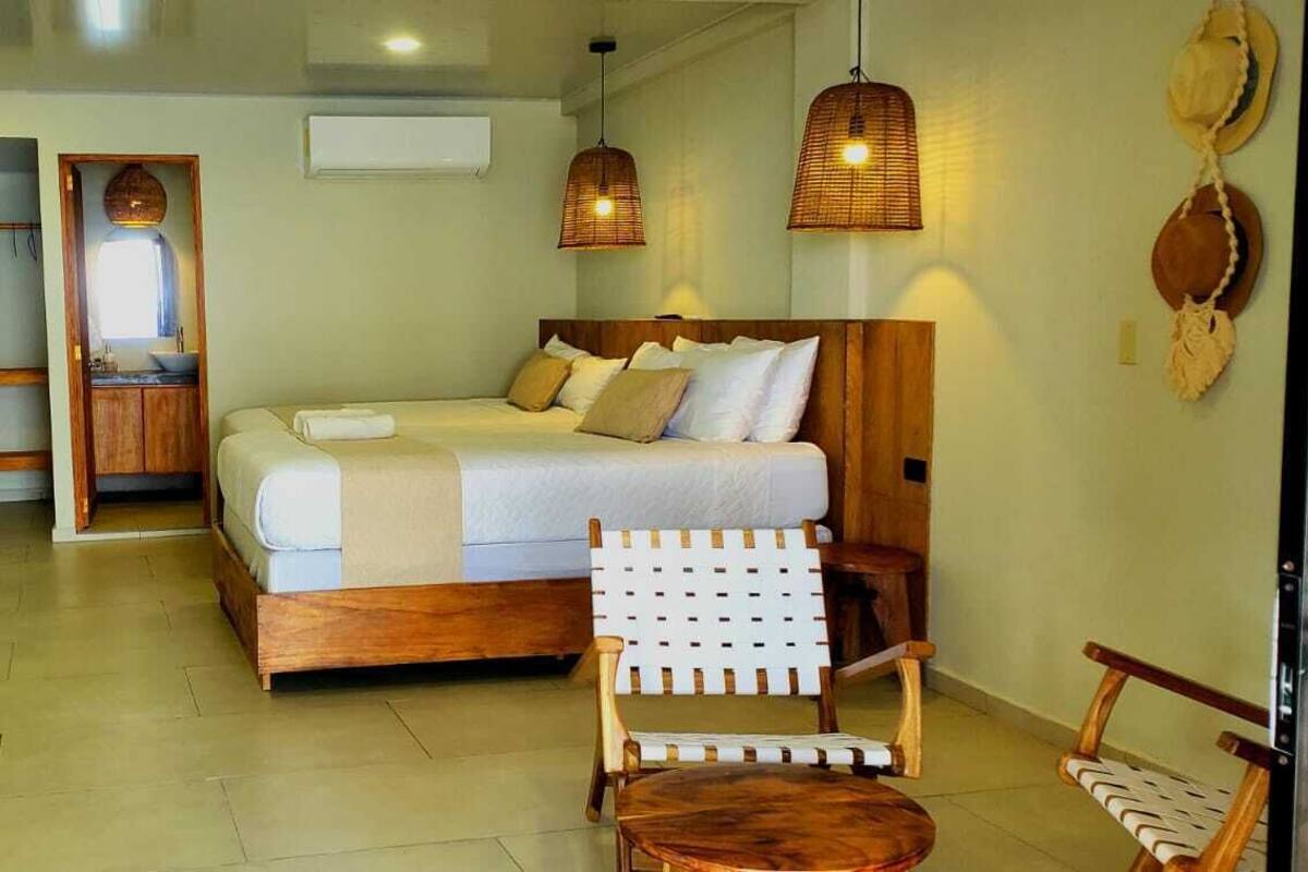 A bedroom with a wooden bed, a small table, a chair, and a view of the sea through a glass door.