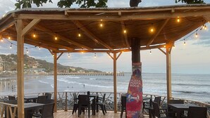 Zona exterior con mesas y sillas, con vista a una playa y al océano.