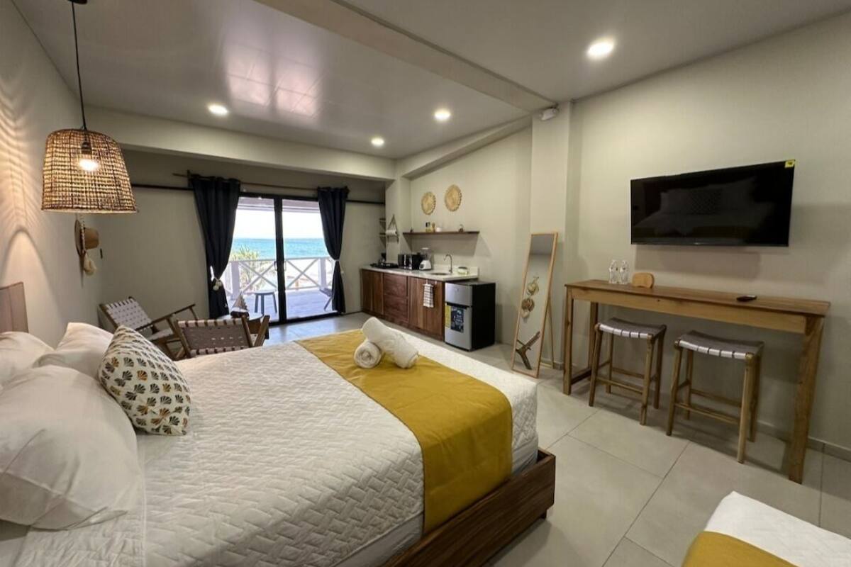 A hotel room with a bed, a desk with a TV, a balcony with a view, and a kitchenette.