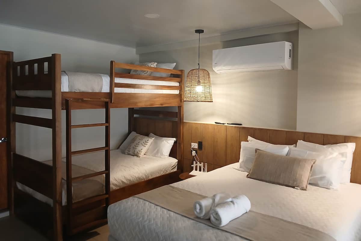 A hotel room with bunk beds, a bed with rolled towels, a hanging light fixture, and an air conditioning unit.