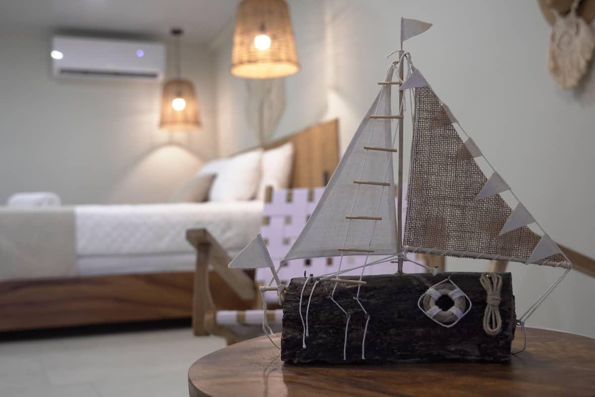 A model sailboat on a wooden table in a bedroom with a bed and two hanging lamps.