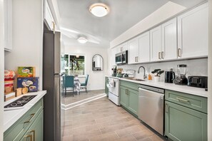 Una cocina moderna con armarios blancos, un microondas y un lavavajillas. Hay un comedor con una mesa y sillas.