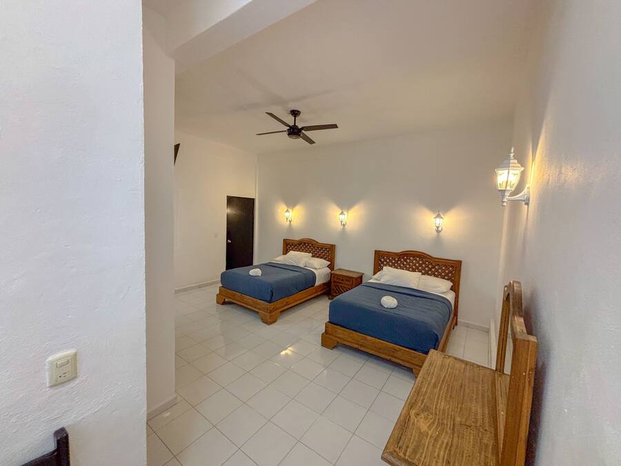 A hotel room with two beds, a ceiling fan, and wall-mounted lights.