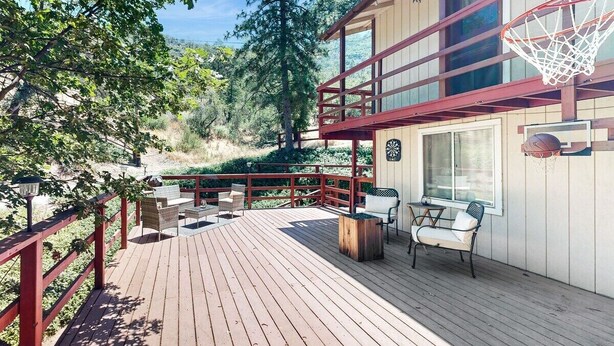 A wooden deck with outdoor furniture, a basketball hoop, and a scenic view of trees and hills. - Spacious home in Sequoia National Forest (California Hot Springs)