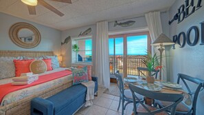 Un dormitorio acogedor con cama, un banco, una mesa de comedor con sillas y vista al océano a través de una puerta corrediza.