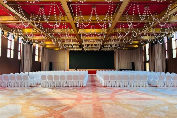 Un salón amplio con filas de sillas blancas, un escenario y suelo alfombrado.