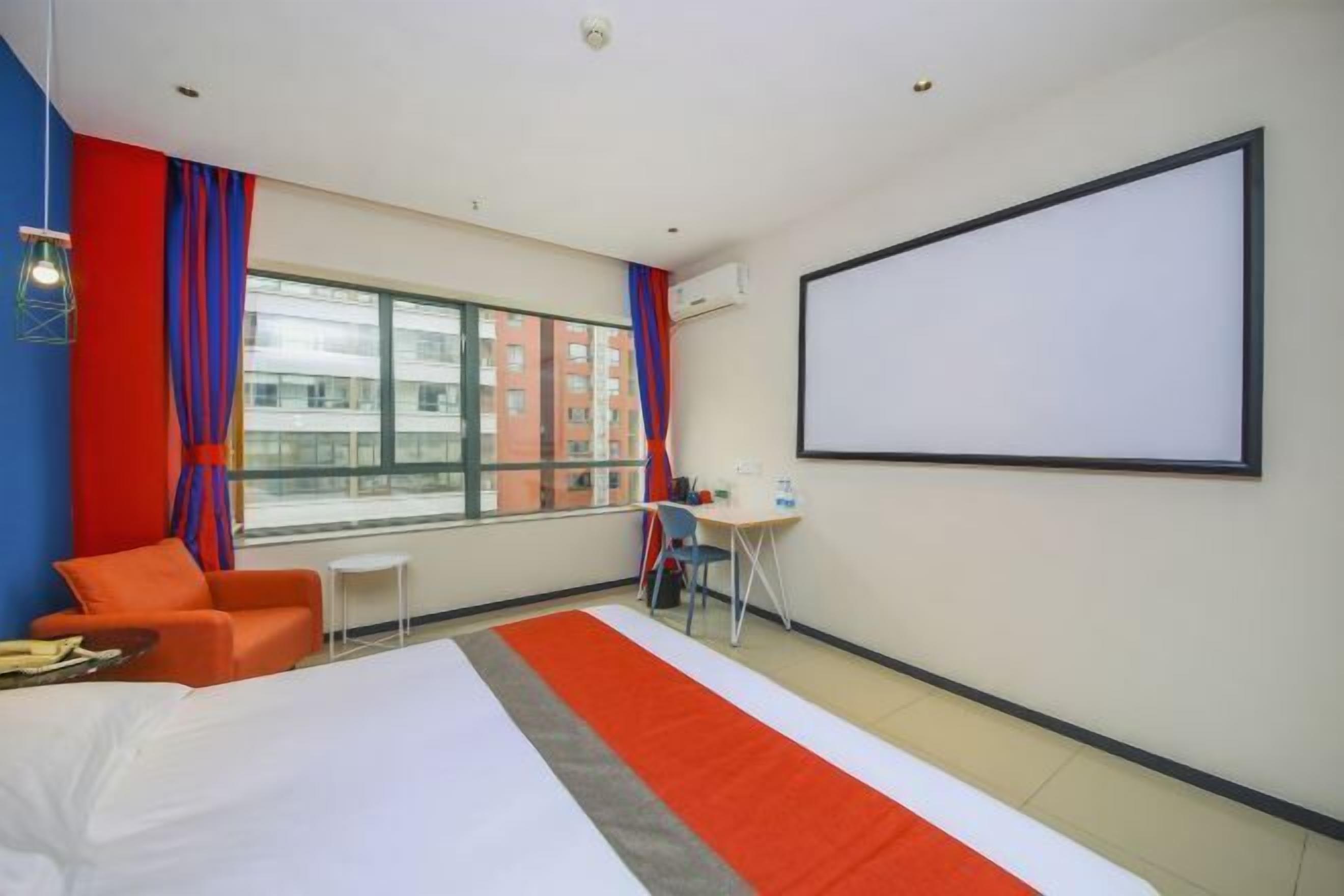 A hotel room with a bed, a desk, a chair, a large window, and a projector screen.