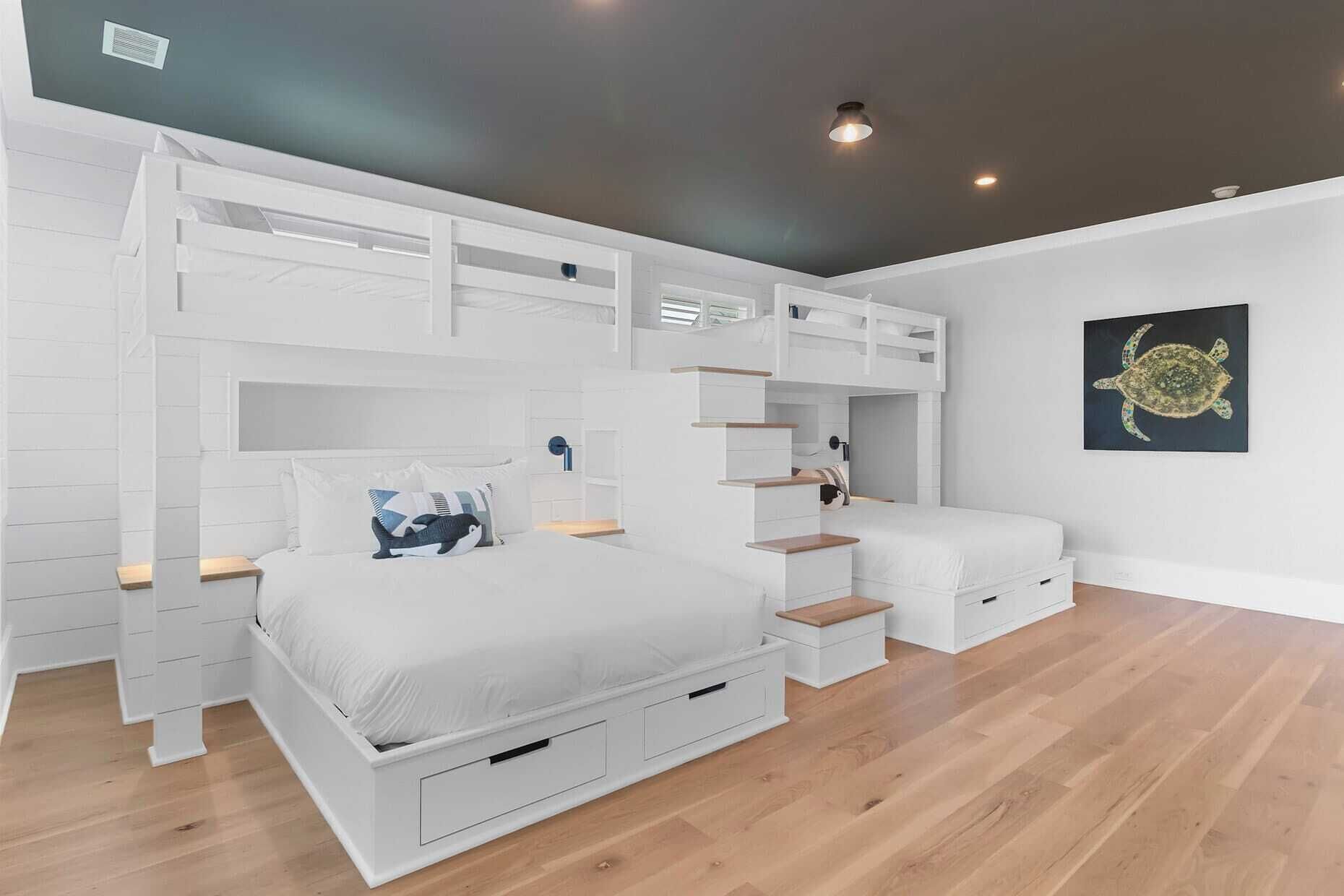 A bunk bed room with a white color scheme, wooden flooring, and a ceiling light fixture.
