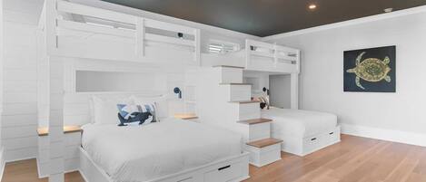 A bunk bed room with a white color scheme, wooden flooring, and a ceiling light fixture.