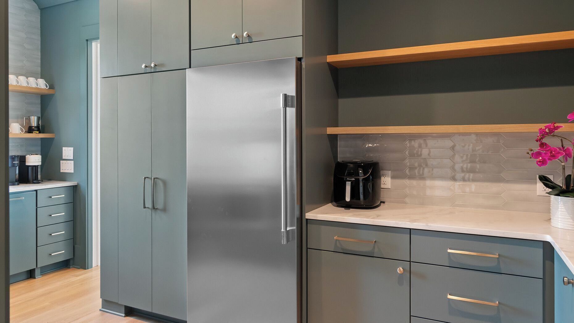 Una cocina moderna con armarios grises, un refrigerador de acero inoxidable y una cafetera sobre la encimera.