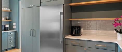 Una cocina moderna con armarios grises, un refrigerador de acero inoxidable y una cafetera sobre la encimera.