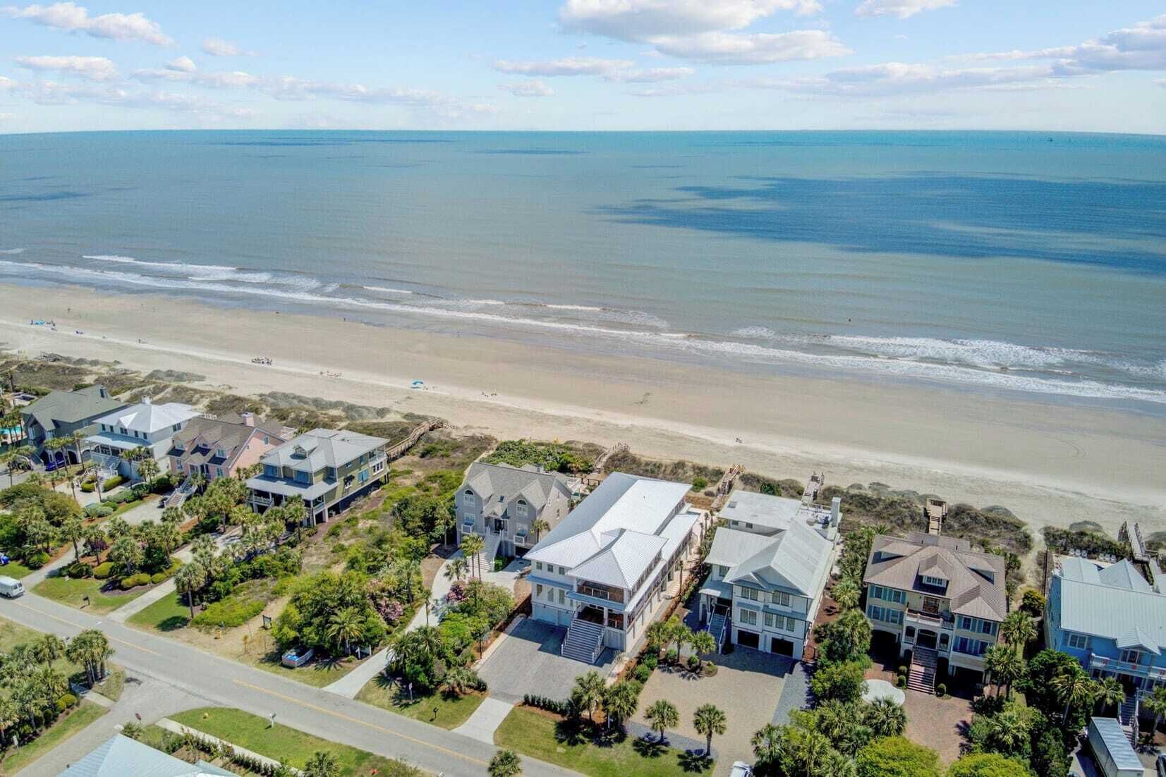 A coastal residential area with beachfront properties, including houses with large windows and balconies, and a road leading to the beach.