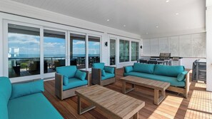 A spacious outdoor area with wooden flooring, teal sofas, and a barbecue grill. - 712 Ocean Blvd by Avantstay New Construction w/ Pool, Game Zone, Private Beach Access, and Oceanfront Views (Isle of Palms)