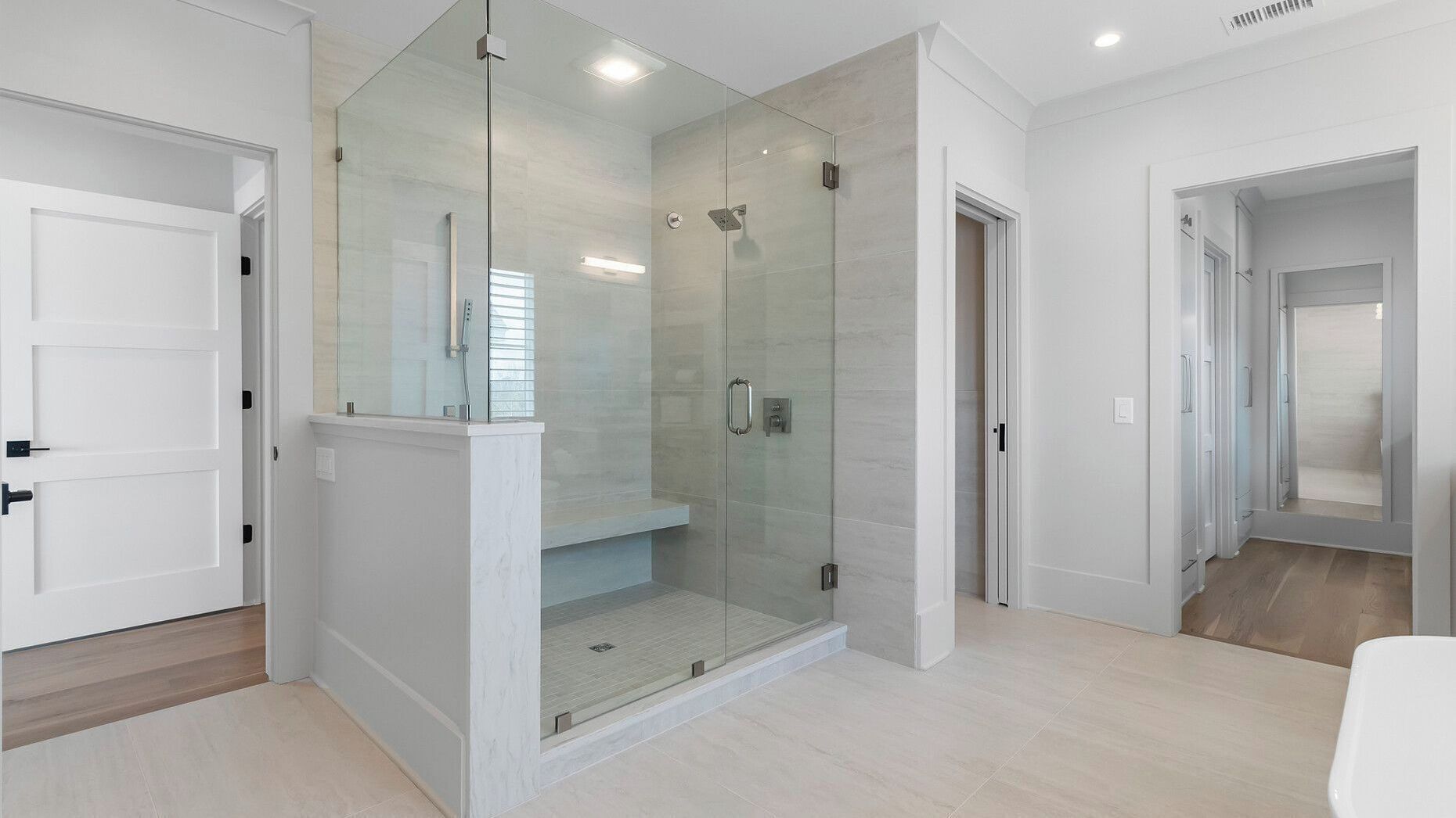 A modern bathroom with a glass-enclosed shower, white walls, and a wooden floor.