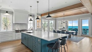 A modern kitchen with a large island, pendant lights, and a view of the ocean. - 712 Ocean Blvd by Avantstay New Construction w/ Pool, Game Zone, Private Beach Access, and Oceanfront Views (Isle of Palms)