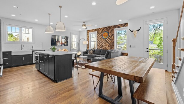 Una cocina moderna con una isla central, un comedor con mesa de madera y un espacio de sala con sofá y decoración en la pared.