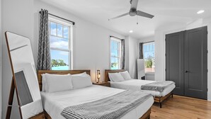 Habitación de hotel con dos camas, ventilador de techo y ventanas amplias.