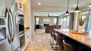 A modern kitchen with a large island, bar stools, and a dining area with a sofa and chairs. - Spacious 5-bedroom house in fabulous Queen Creek with WiFi, AC (Queen Creek)