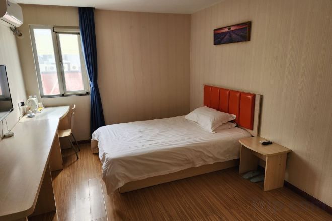 Habitació d'hotel amb llit, escriptori, cadira, taula petita i finestra amb cortines.