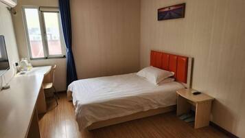 Habitació d'hotel amb llit, escriptori, cadira, taula petita i finestra amb cortines.