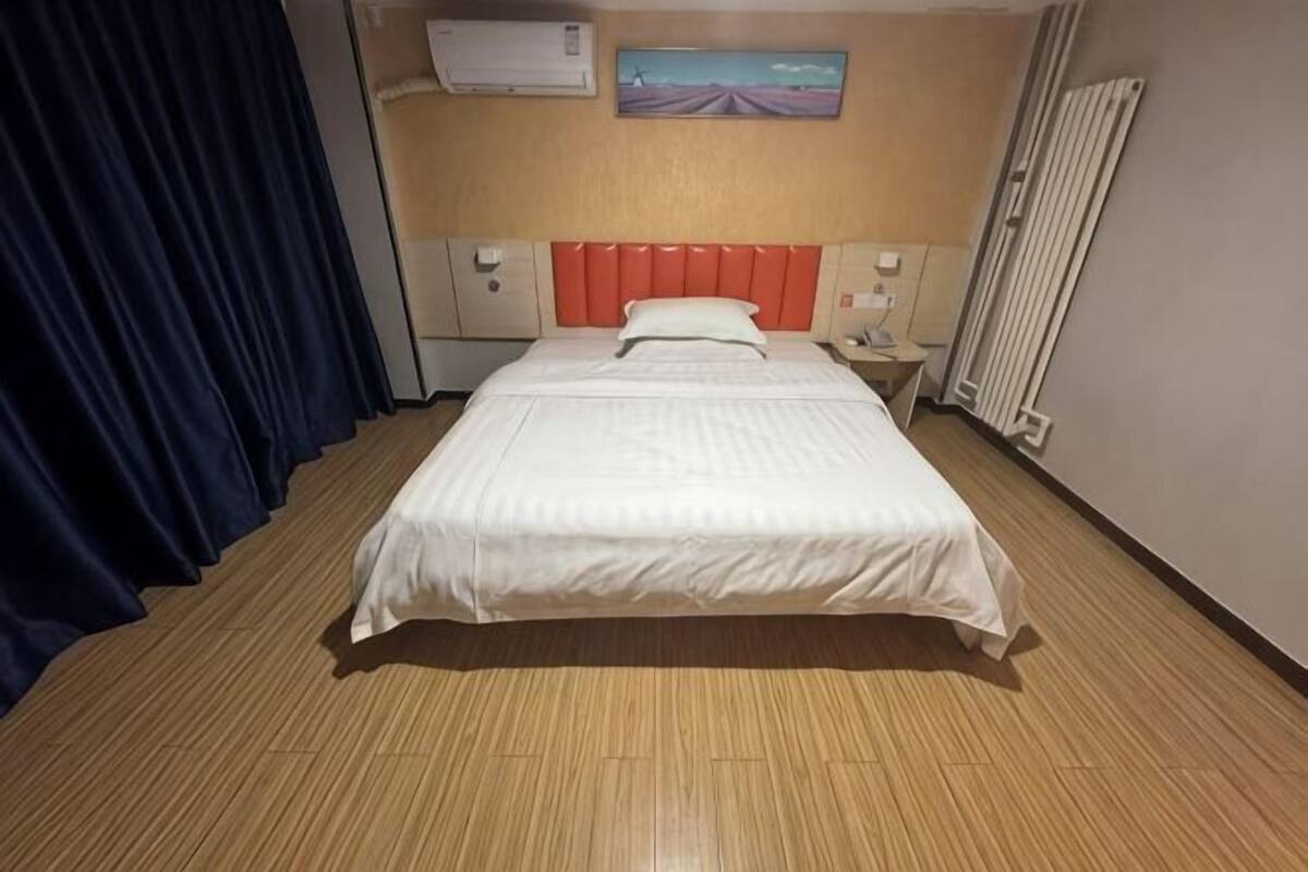 Ein Hotelzimmer mit Bett, Nachttisch, Klimaanlage, Heizkörper und einem Bild an der Wand.