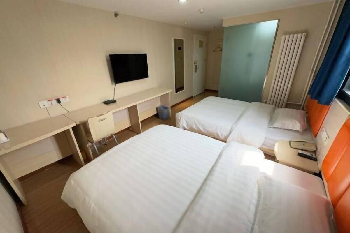 Ein Hotelzimmer mit zwei Betten, einem Schreibtisch, einem Fernseher und einem Fenster mit Vorhängen.