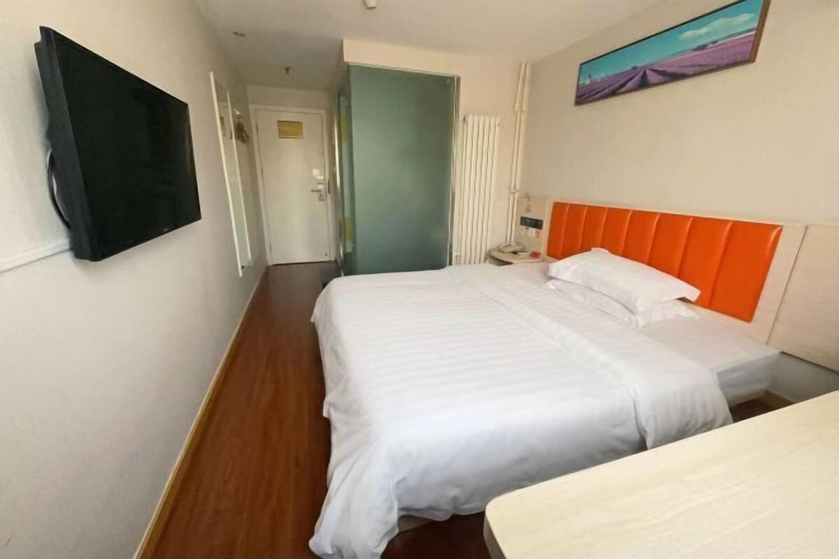 Ein Hotelzimmer mit Bett, Nachttisch, einem an der Wand montierten Flachbildfernseher und einem Gemälde über dem Bett.
