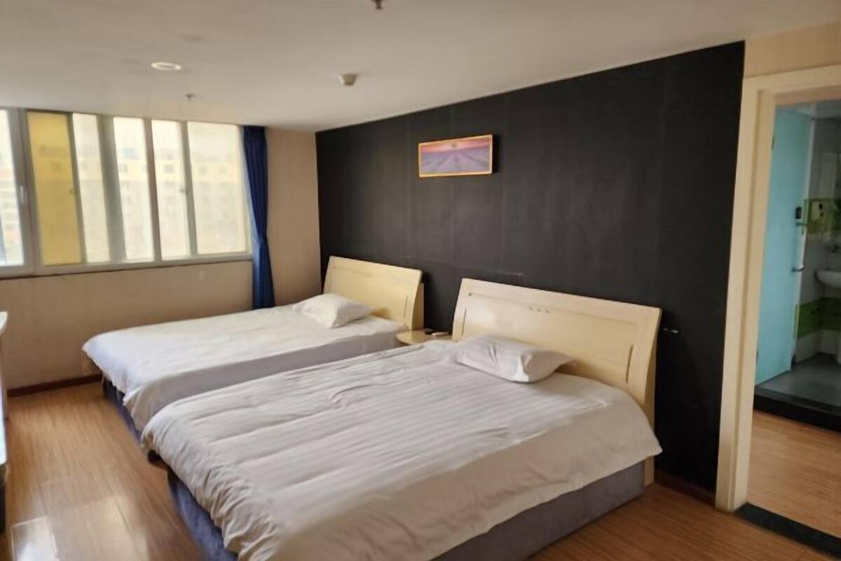 Ein Hotelzimmer mit zwei Betten, einer dunklen Wand, einem Fenster mit Vorhängen und einem kleinen Gemälde.