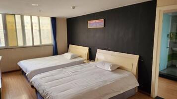 A hotel room with two beds, a dark wall, a window with curtains, and a small painting.