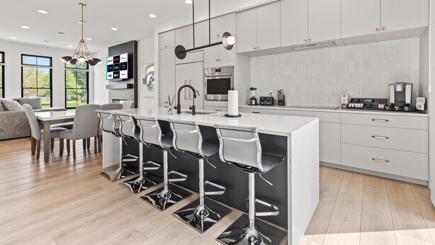 A modern kitchen with a central island, bar stools, and a dining area with a sofa and table.